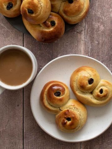 Lussekatter on a plate, with a cup of coffee on the side.