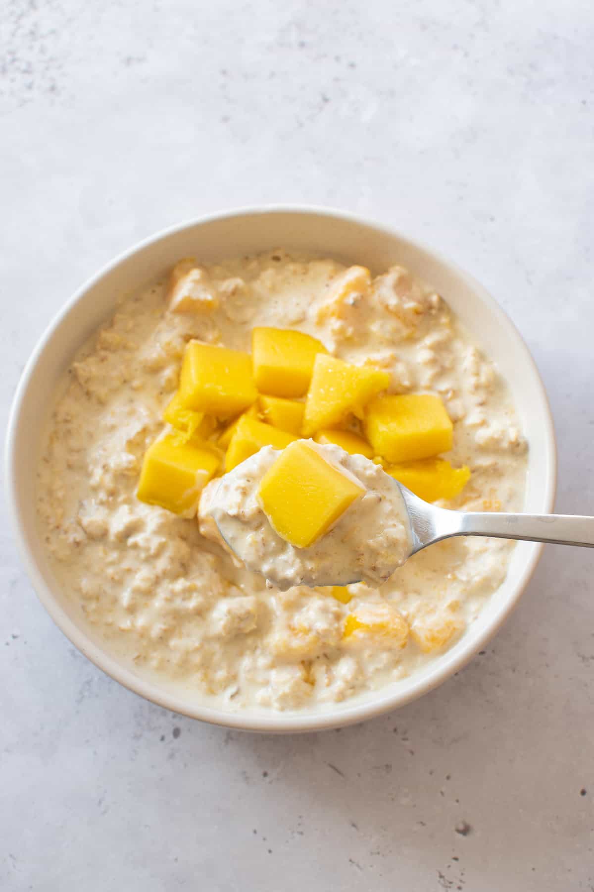 Mango overnight oats in a bowl. A spoon is lifting up a serving.