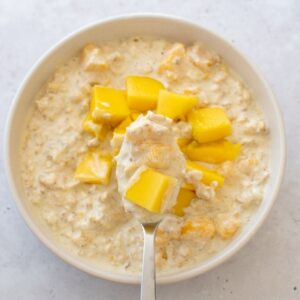 A spoon filled with creamy mango oats.