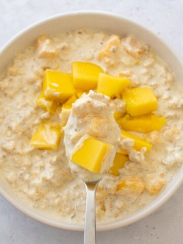 A spoon filled with creamy mango oats.