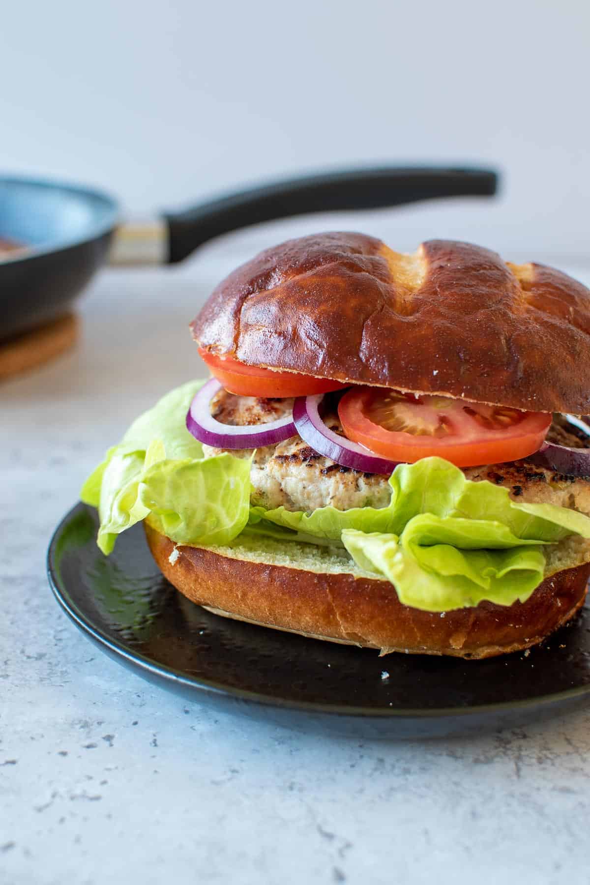 A burger on a plate, with a frying pan in the background.