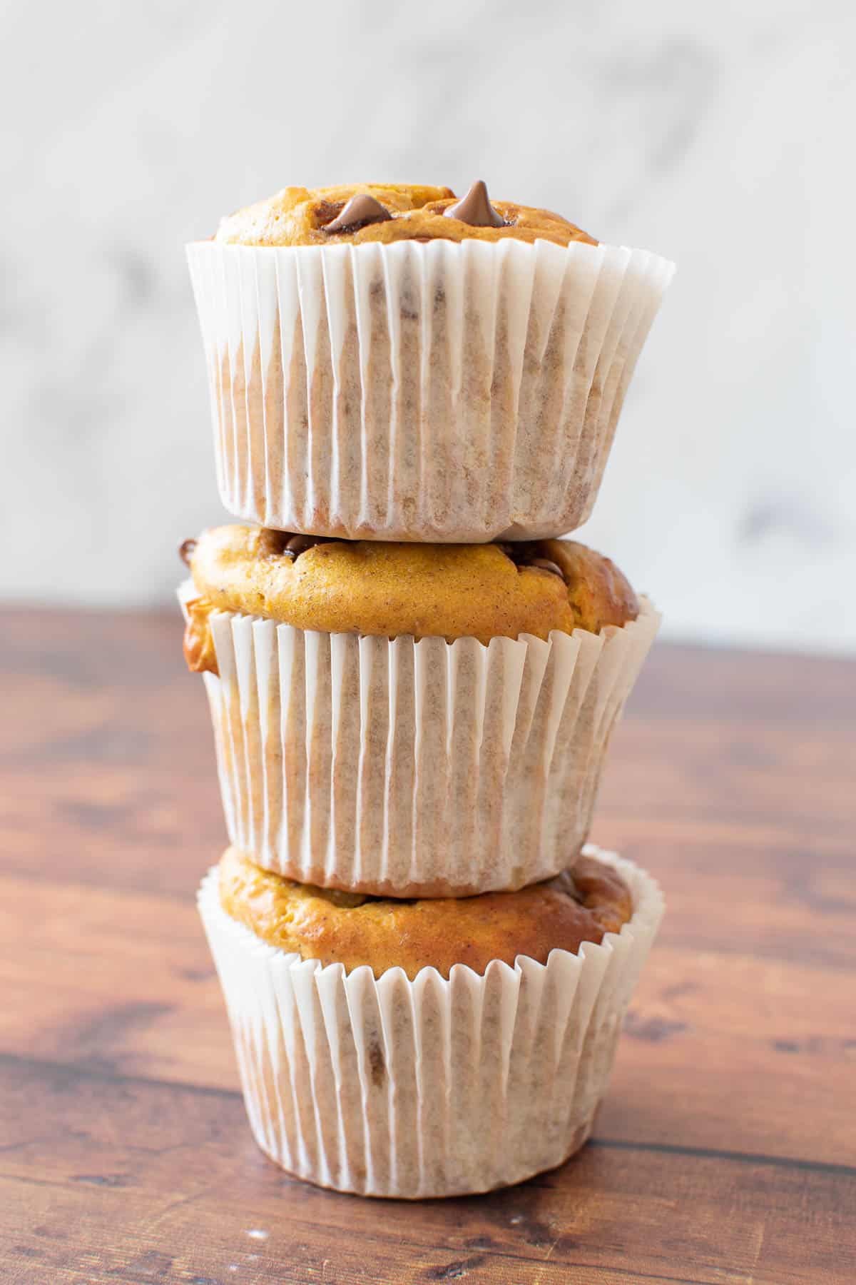 Three pumpkin chocolate chip muffins stacked on top of each other.