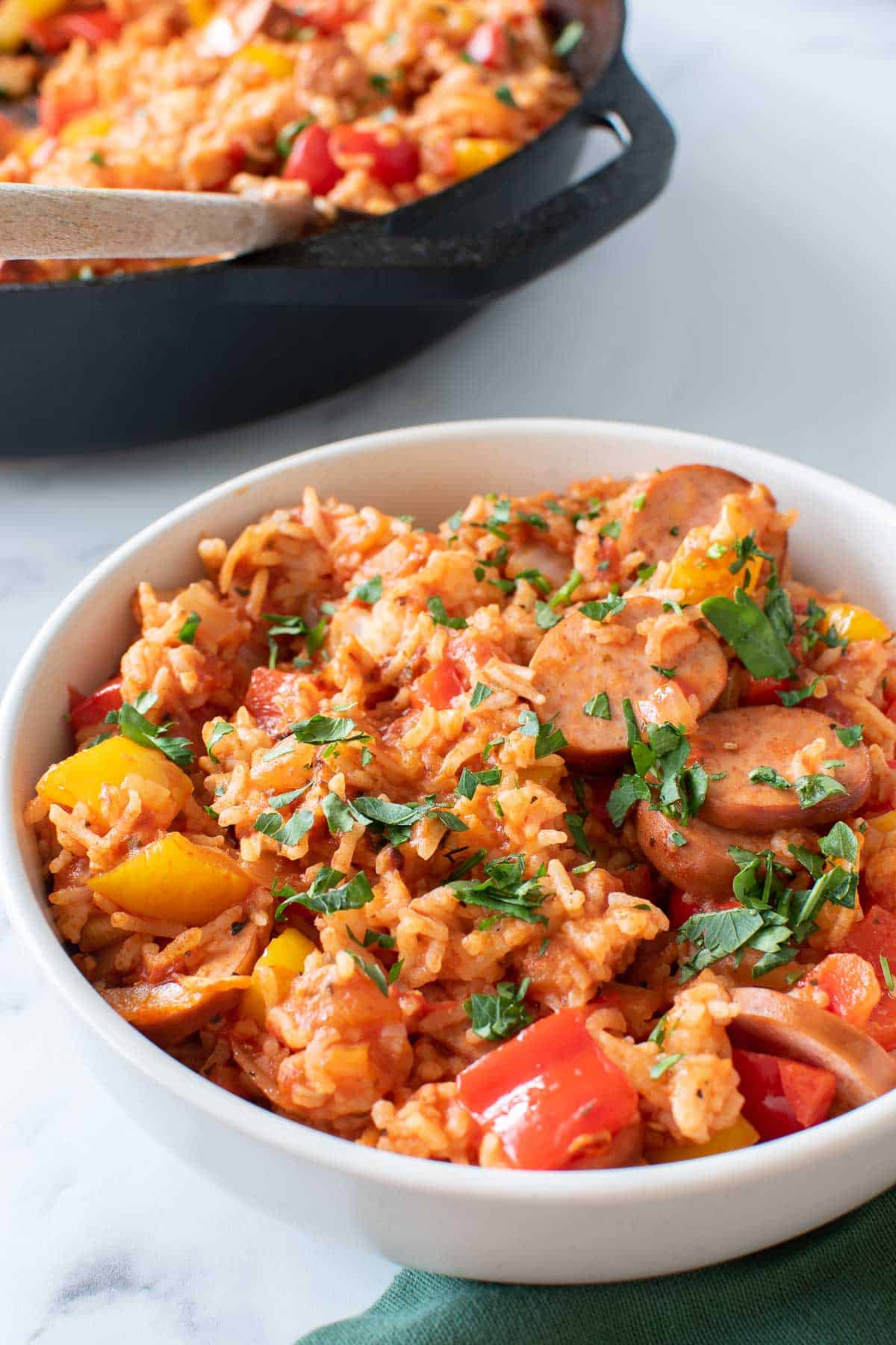 A bowl of sausage and rice casserole, with a cast iron pan in the background.