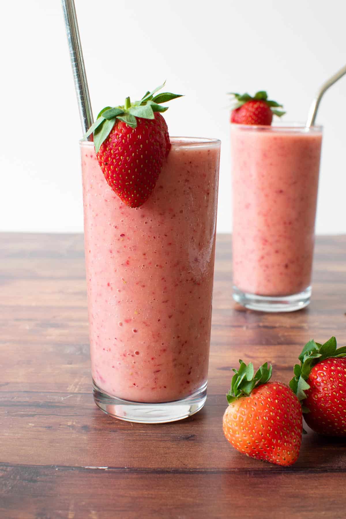 Two glasses of peach and strawberry smoothie, decorated with fresh strawberries.