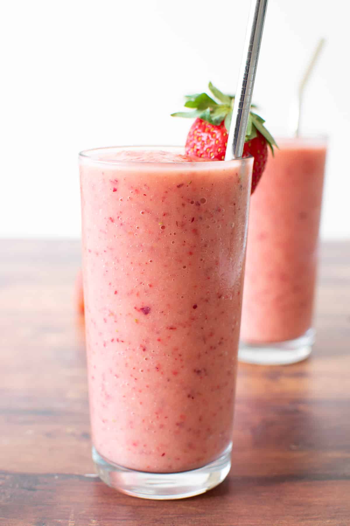 A glass of smoothie with strawberries and peaches, with metal straws inserted.