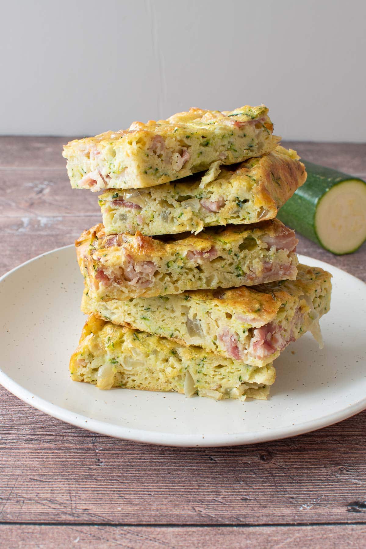 A plate of stacked zucchini slices, with zucchini in the background.