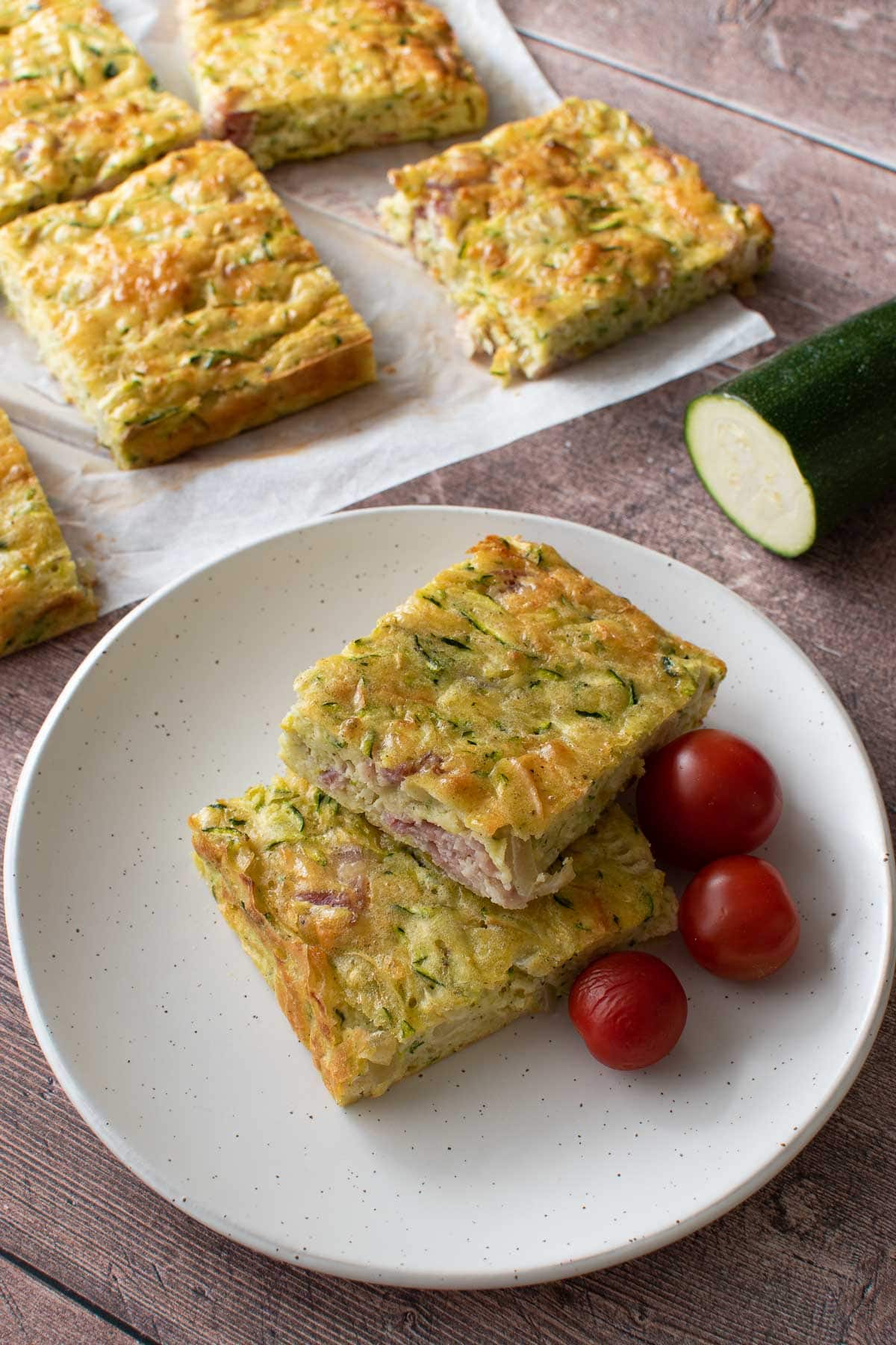 A plate with zucchini and bacon slices, with tomatoes on the side.