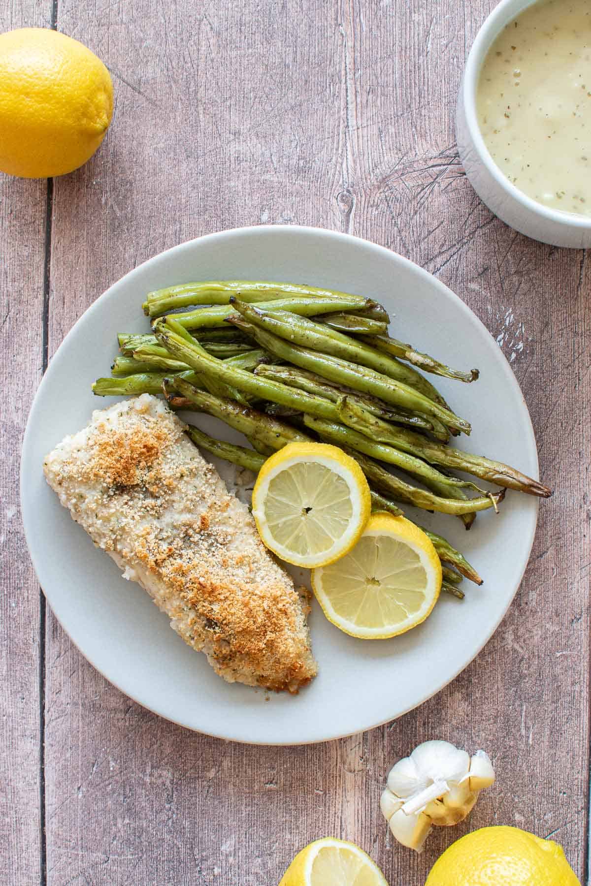 A dinner plate with haddock, green beans and lemon.