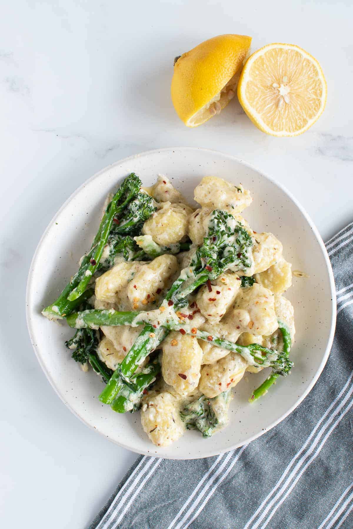 Gnocchi and broccoli on a plate, with lemon on the side.