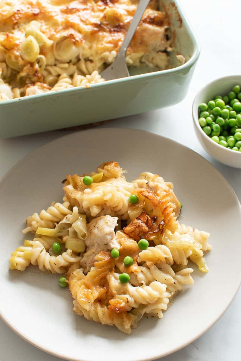 A plate of pasta bake with chicken, leek and peas, with peas and pasta bake in the background.