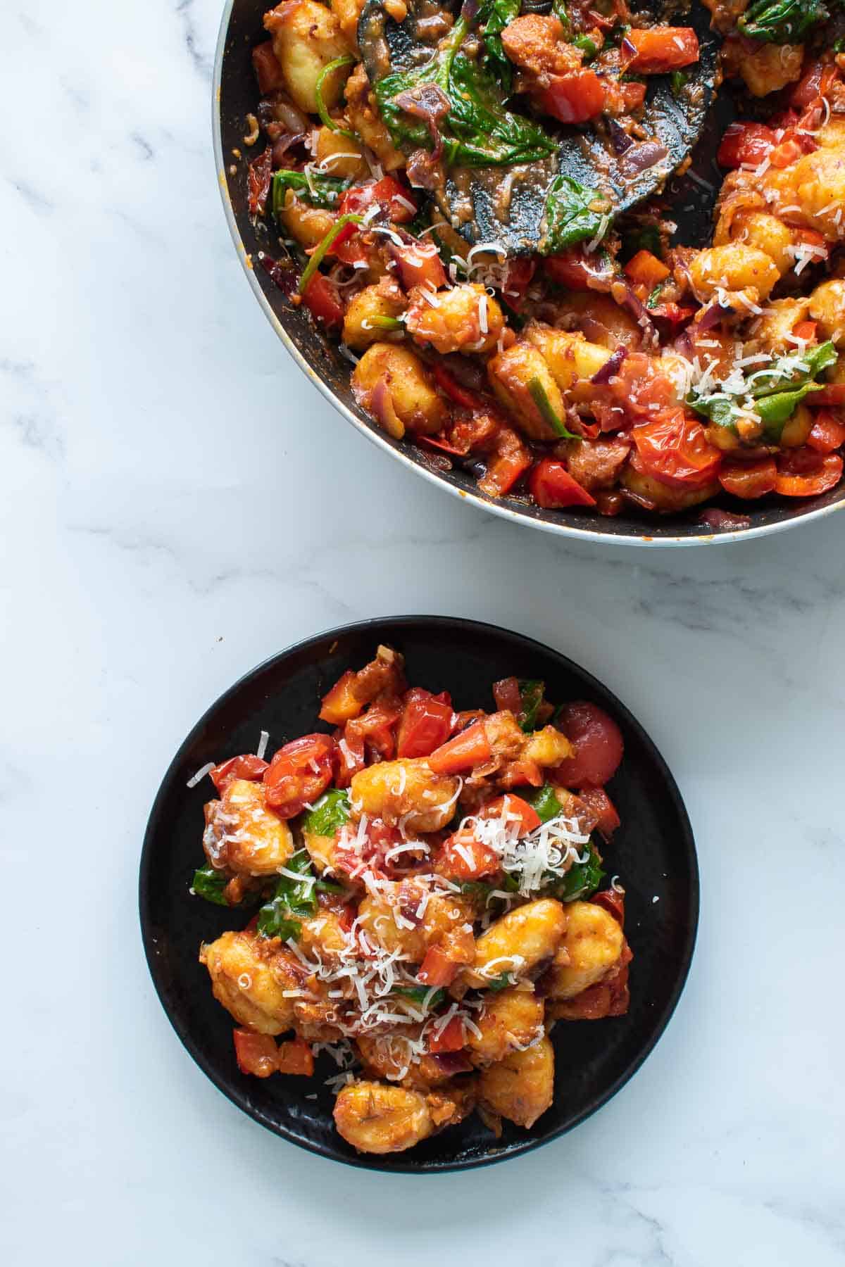 A skillet and a plate with gnocchi with chorizo.