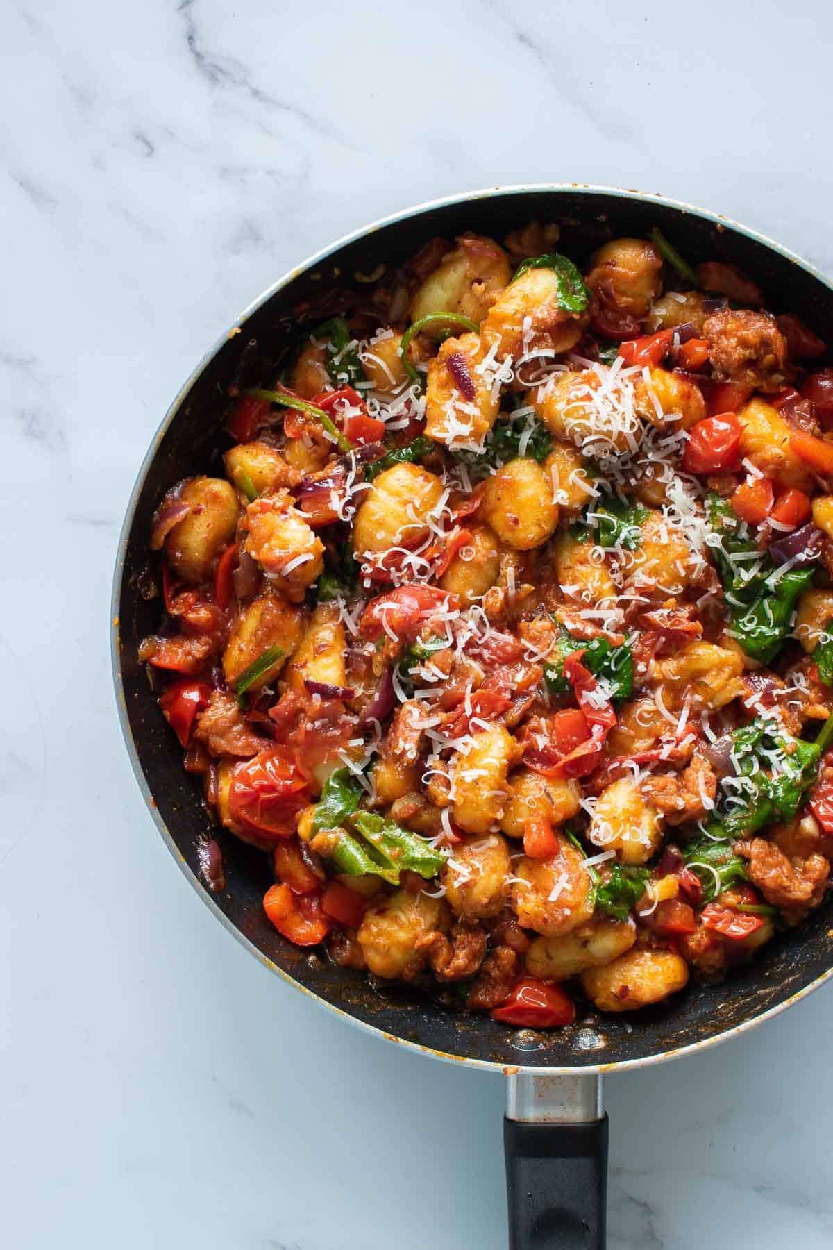 A skillet with tomatoes, chorizo sausage, gnocchi, spinach and peppers.