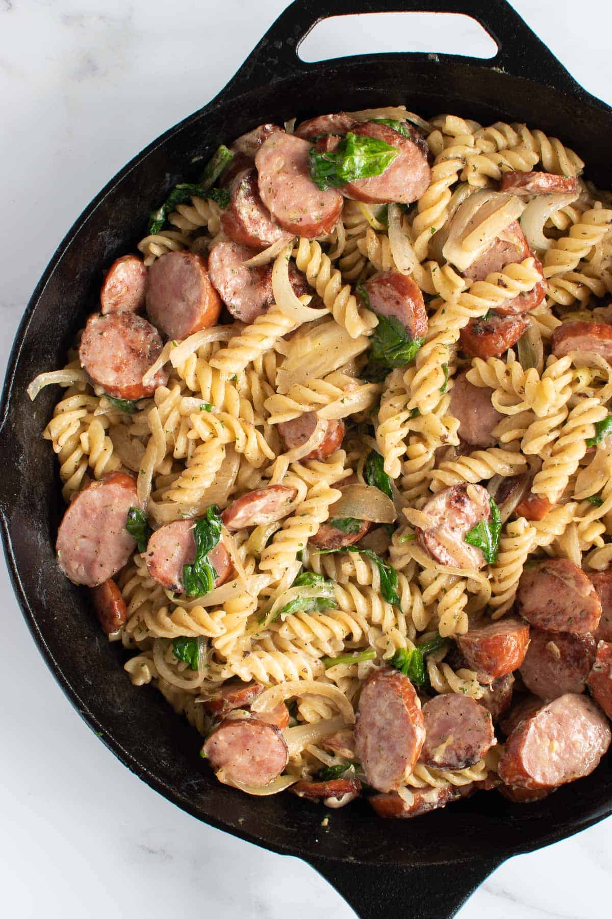 A skillet with sliced kielbasa sausage and fusilli.