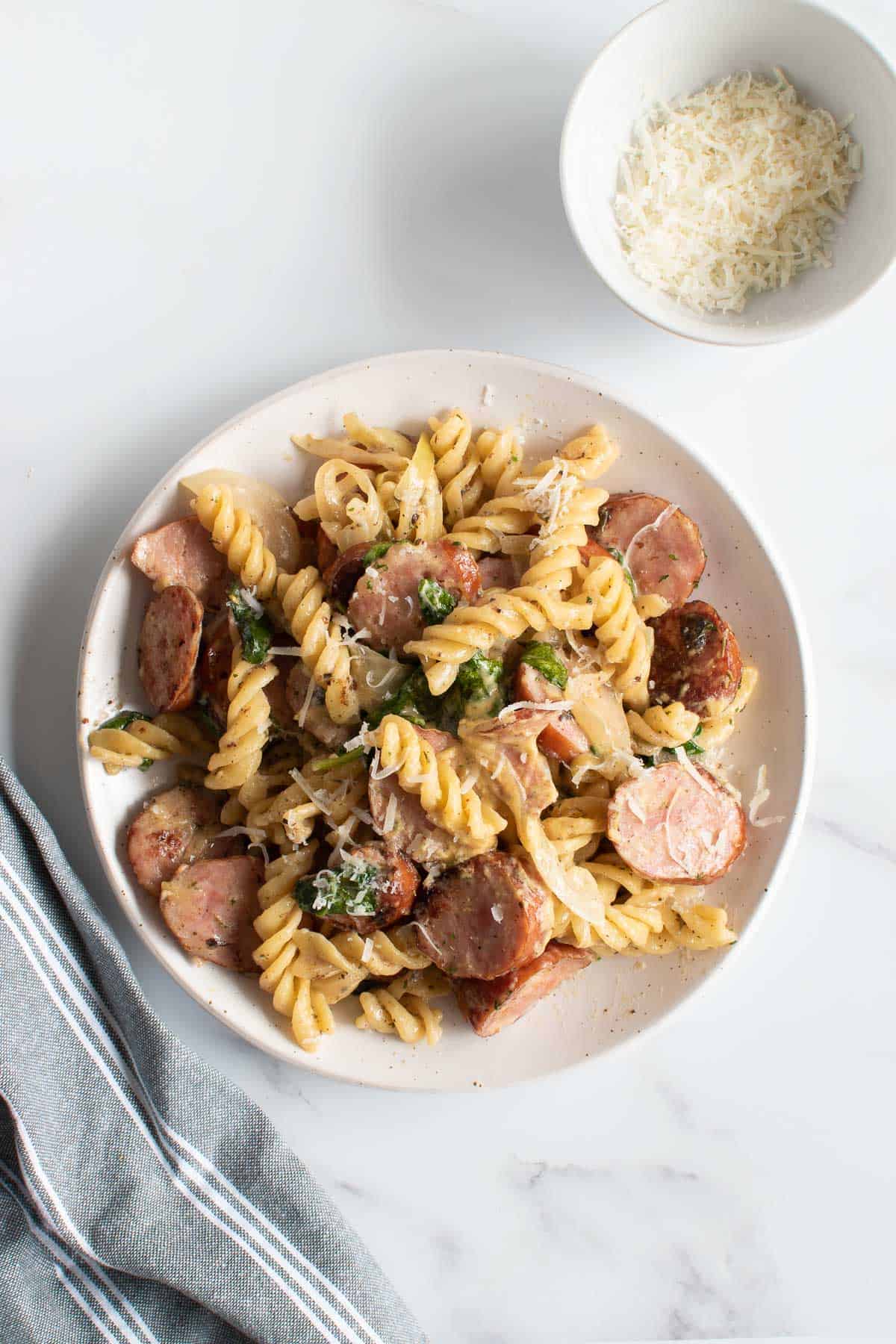 A plate of kielbasa pasta with Parmesan on the side.