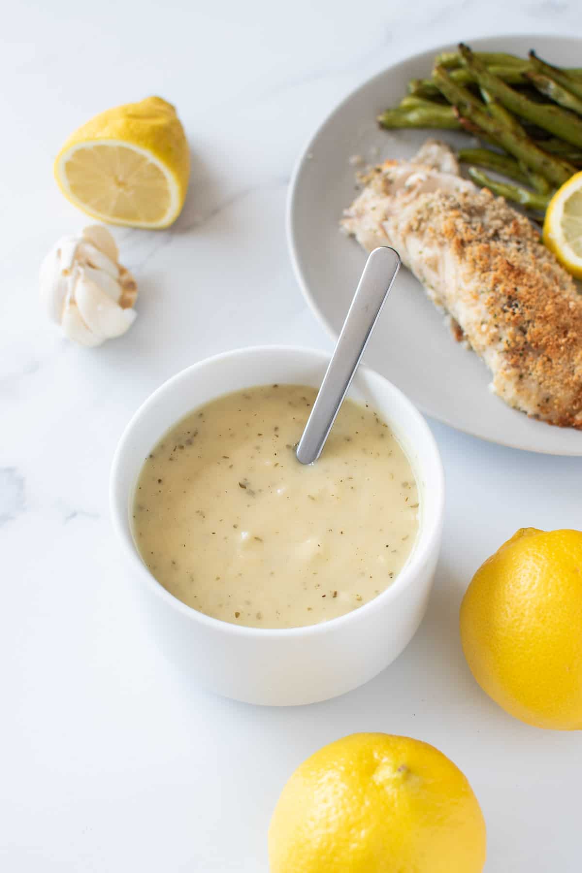 A bowl of lemon garlic sauce with fish and lemon on the side.