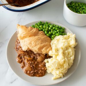 Minced beef puff pastry pie with peas and mashed potatoes.