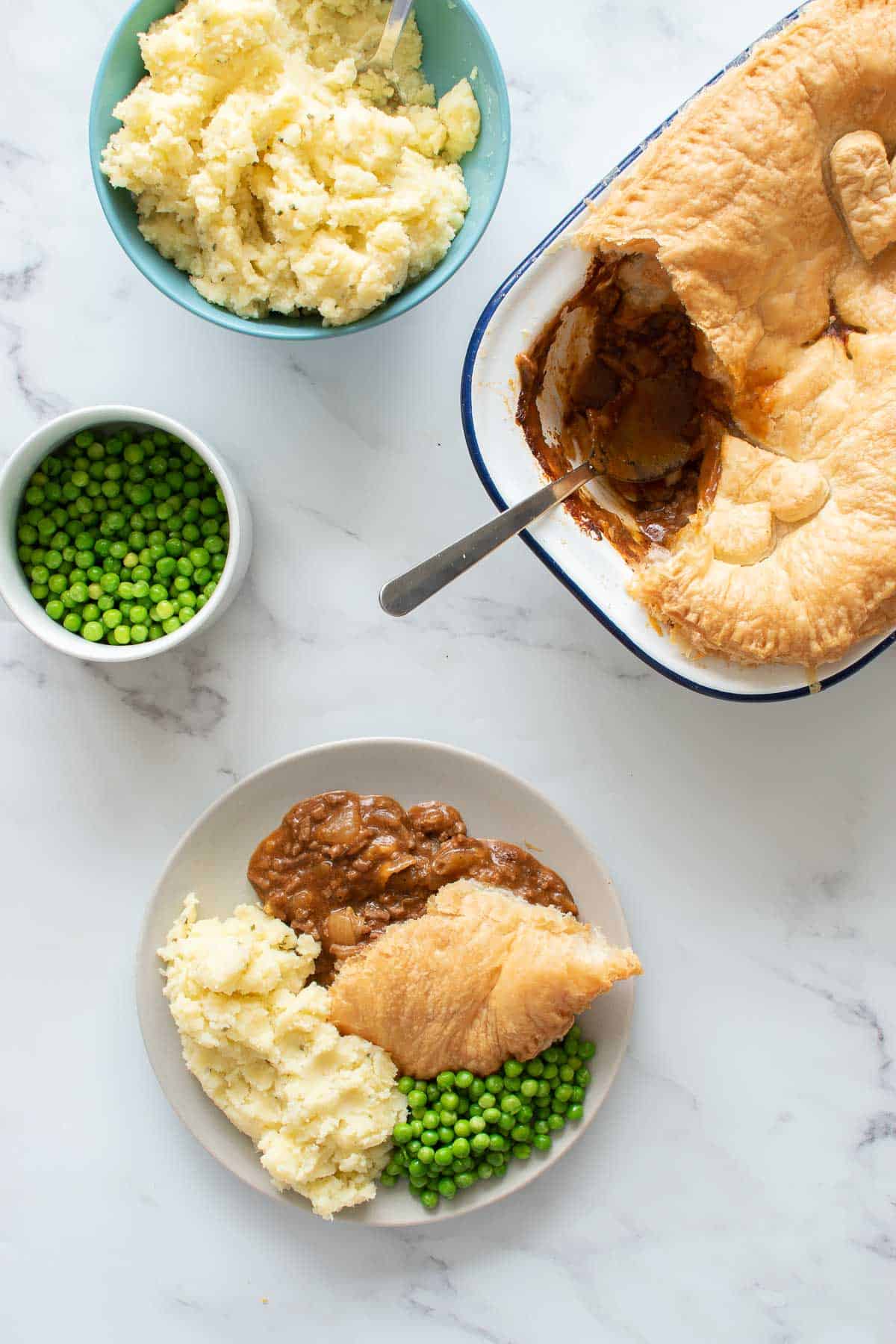 A table with beef pie, mashed potaotes, and peas, and a plate with a full serving.