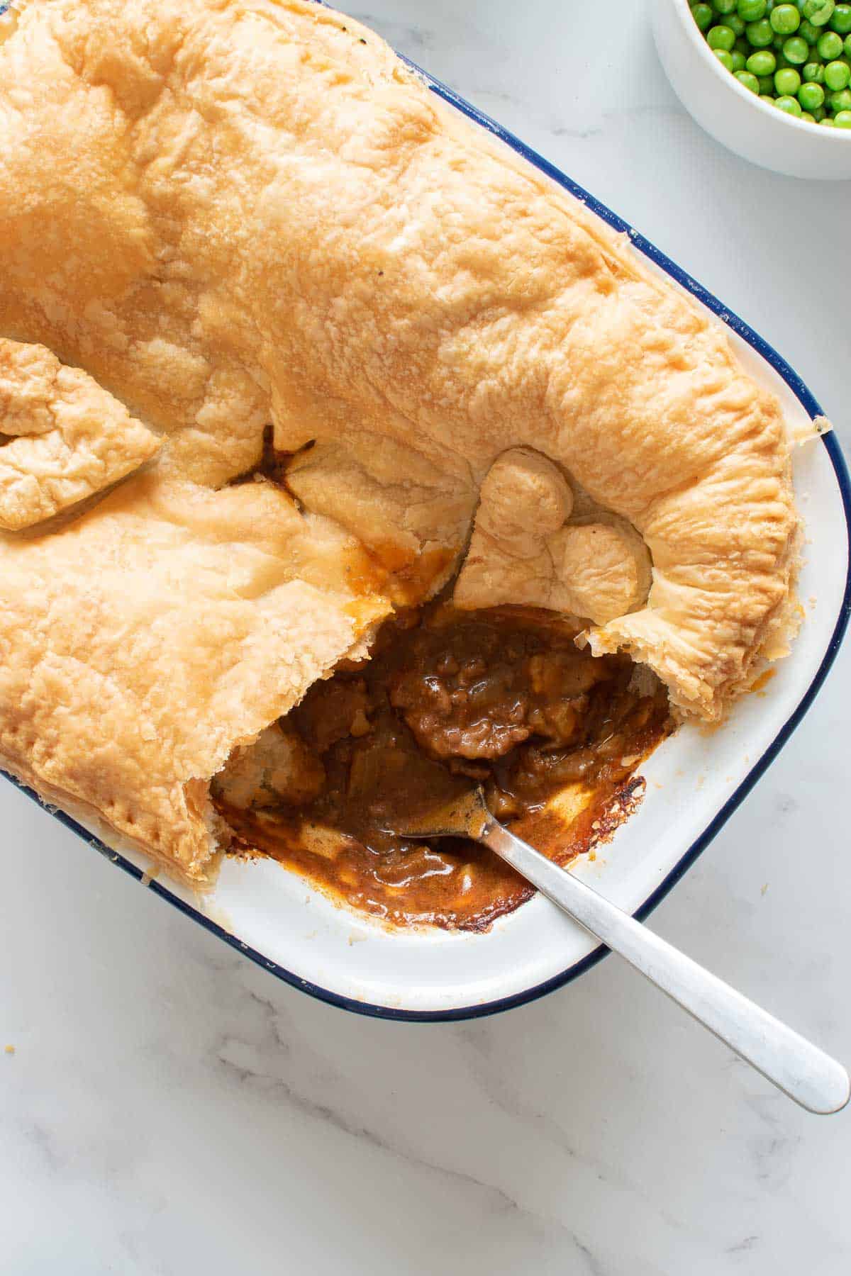 Savory beef pie with puff pastry, with a serving removed.