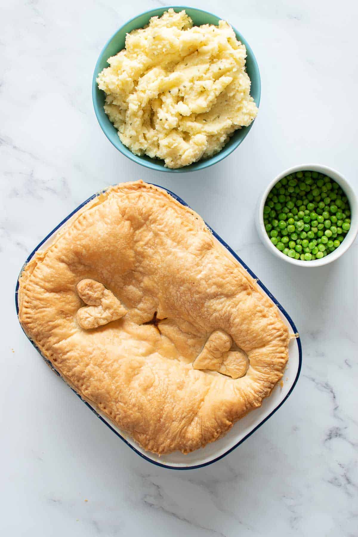 A whole beef pie with mash and peas on the side.