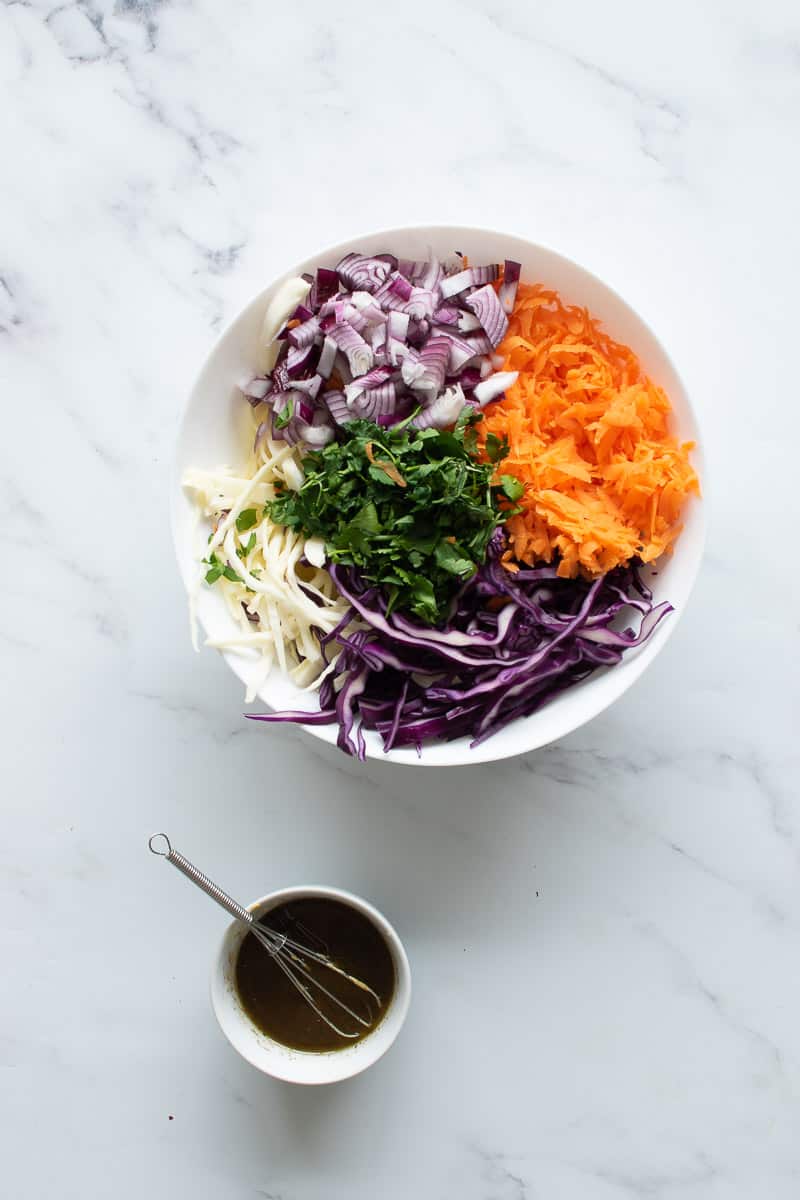 Coleslaw ingredients in a bowl, and a smaller bowl with dressing.