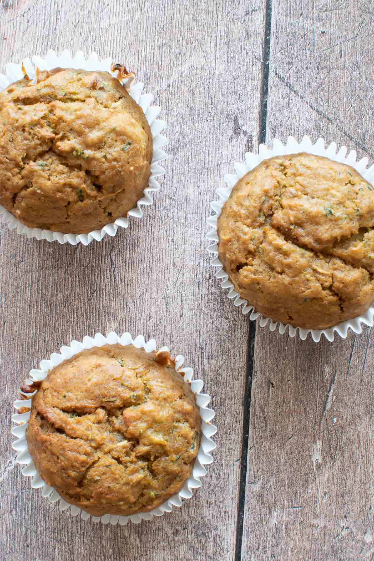 Three pumpkin zucchini muffins on a table.