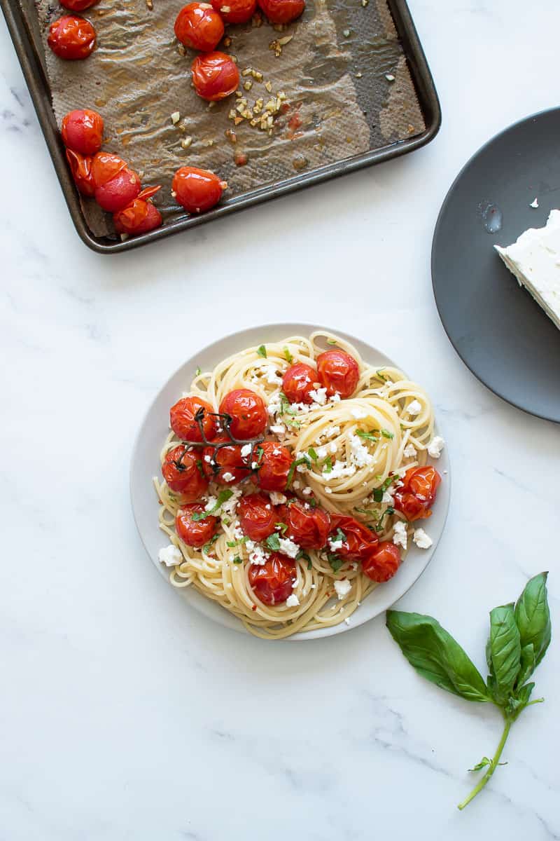 A plate of spaghetti with roasted cherry tomatoes, with roasted tomatoes, feta and basil on the side.