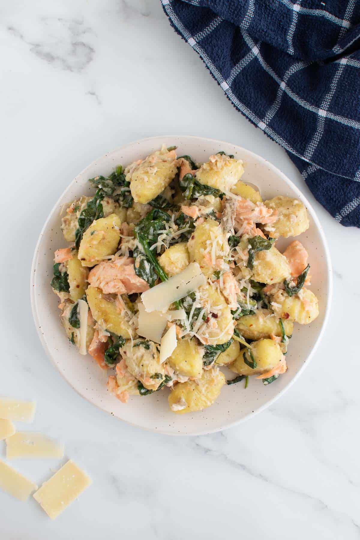 A plate of salmon spinach gnocchi with Parmesan and a tablecloth on the side.