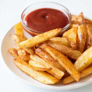 A plate of skin on fries, with a bowl of ketchup on the side.