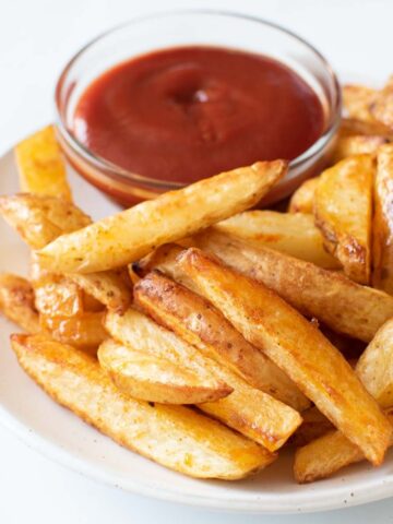 A plate of skin on fries, with a bowl of ketchup on the side.