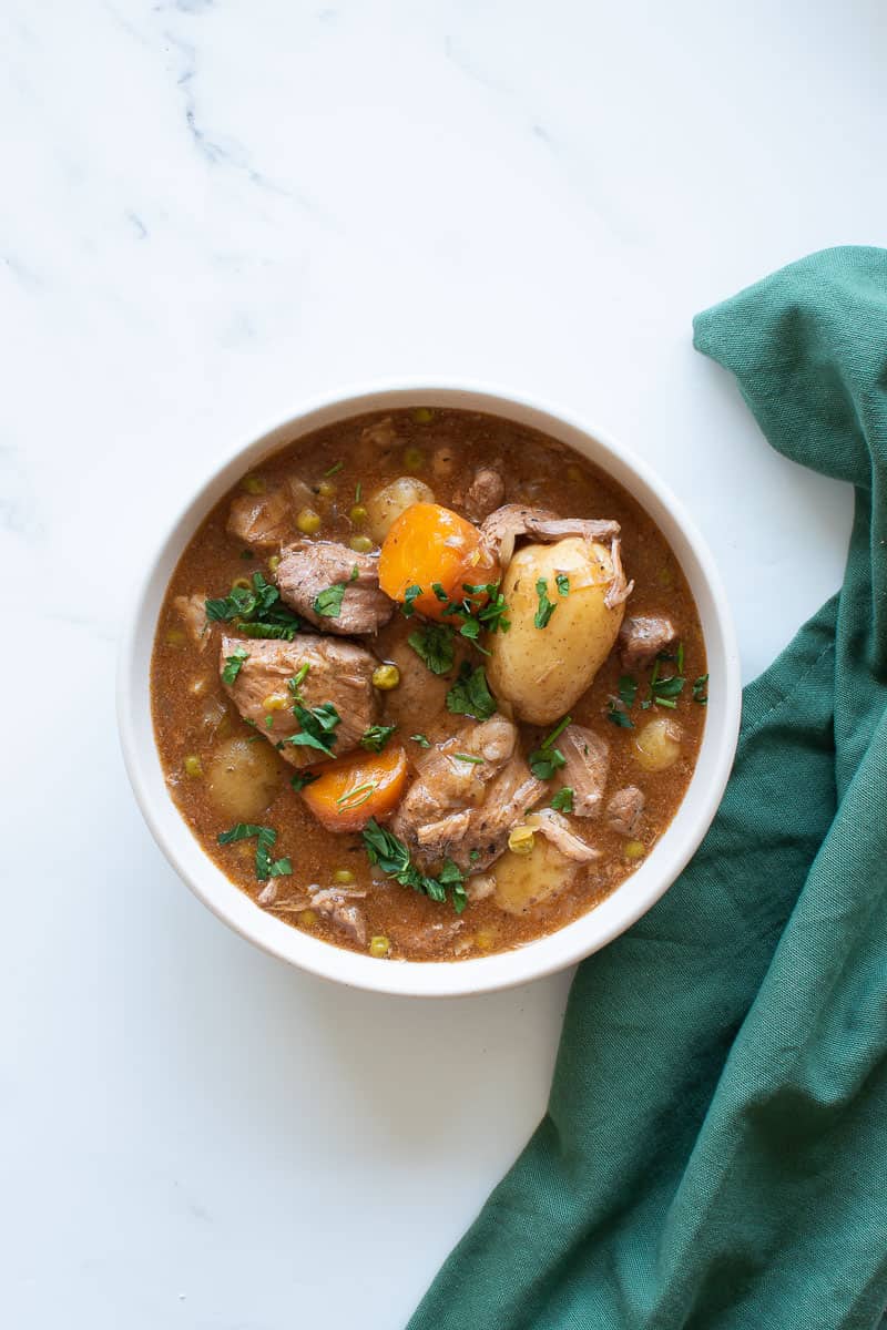 A bowl with pork stew on a table, with a green tablecloth on the side.