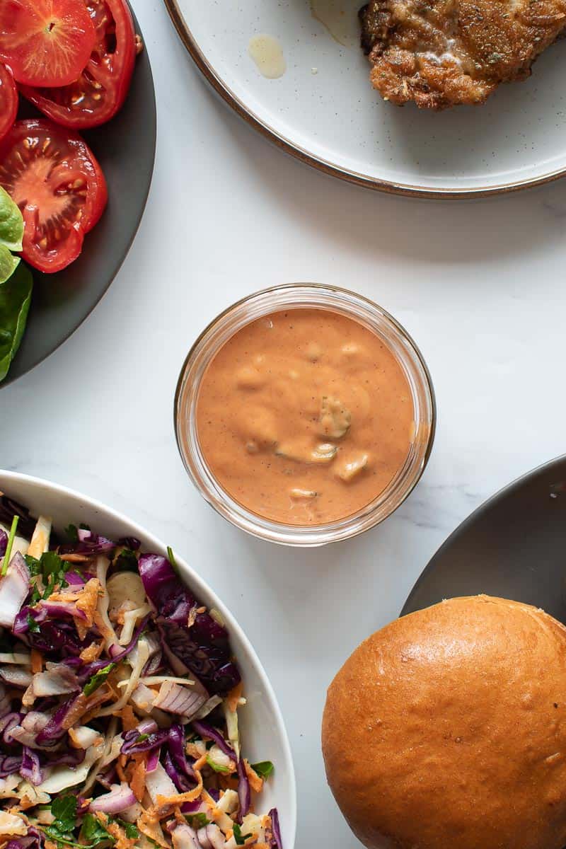 A jar of burger sauce, with burgers and coleslaw on the side.