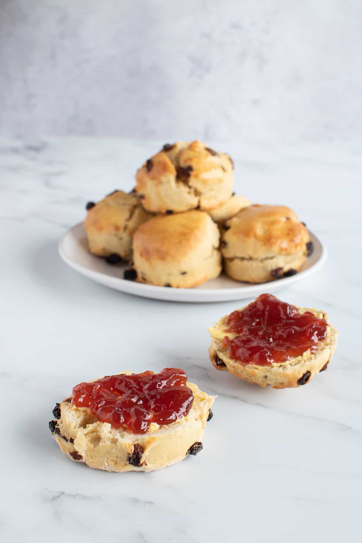 A stack of scones, with a scone sliced in half and filled with jam.
