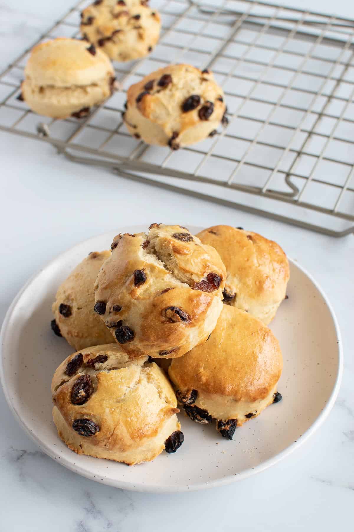 A plate of scones, with more scones resting on a cooling rack in the background.