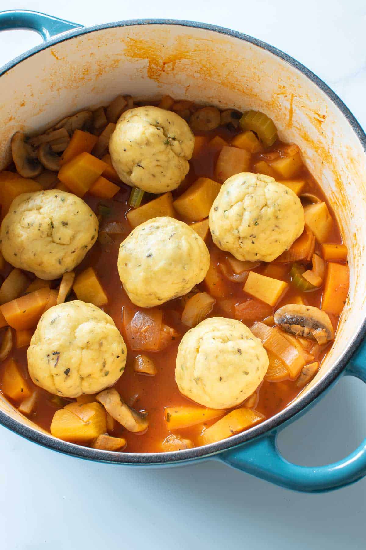 A pot of stew with uncooked dumplings.
