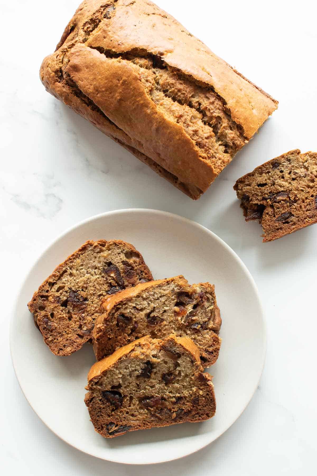 A plate of sliced banana bread, with half a loaf on the side.