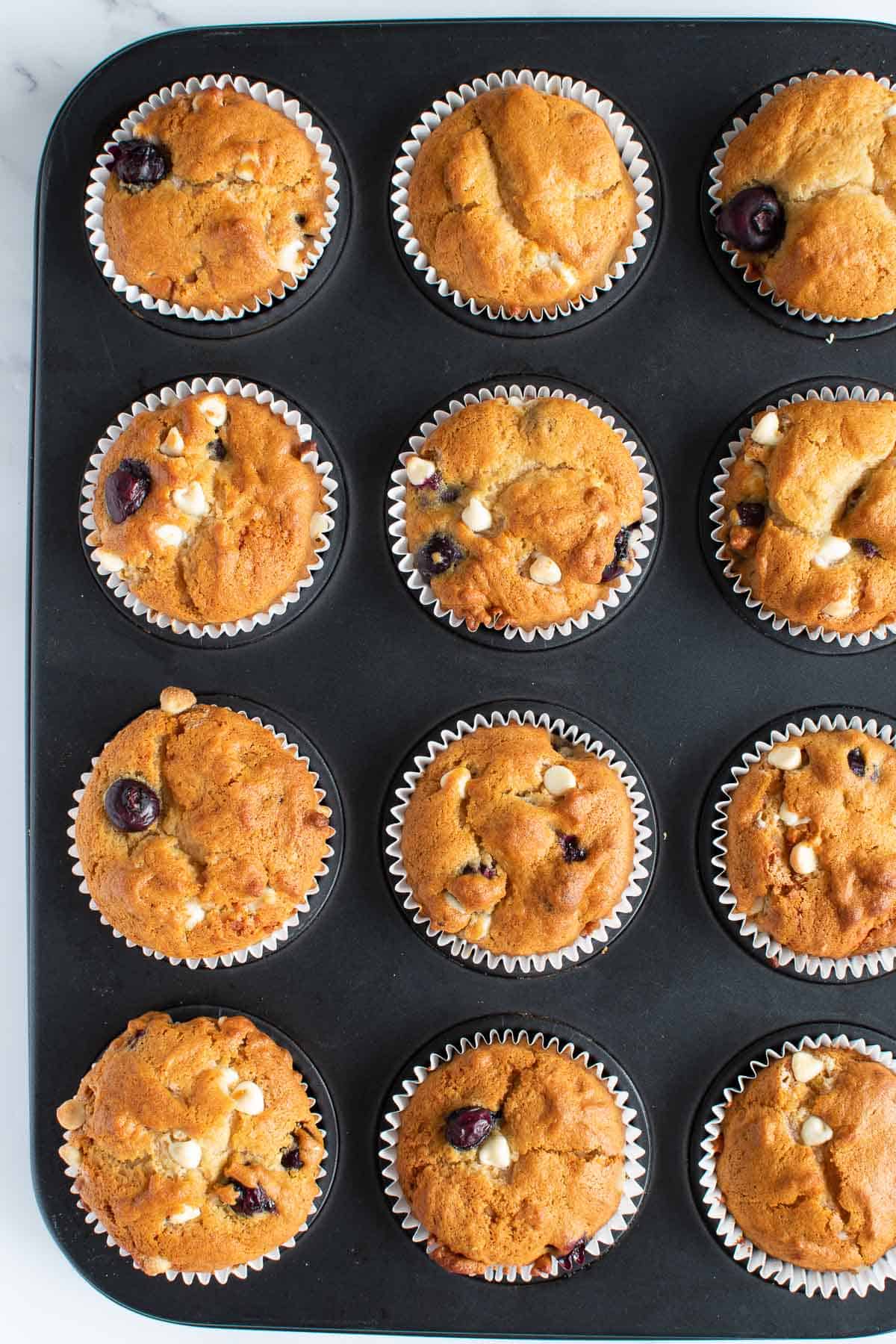 A muffin pan with blueberry white chocolate muffins.