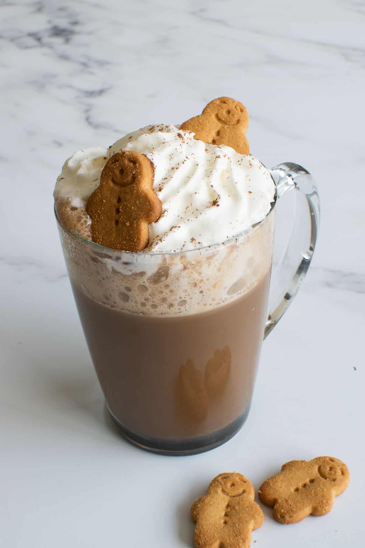 A glass of gingerbread latte with whipped cream and gingerbread men.