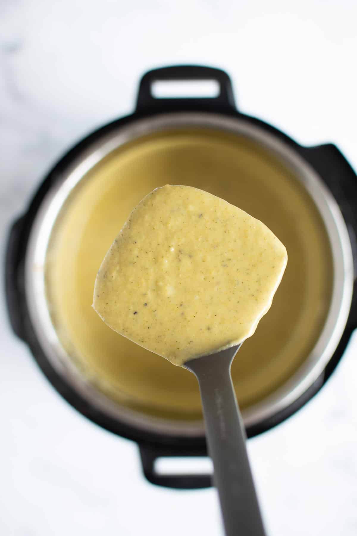 A ladle full of broccoli cheddar soup being lifted above an Instant Pot.