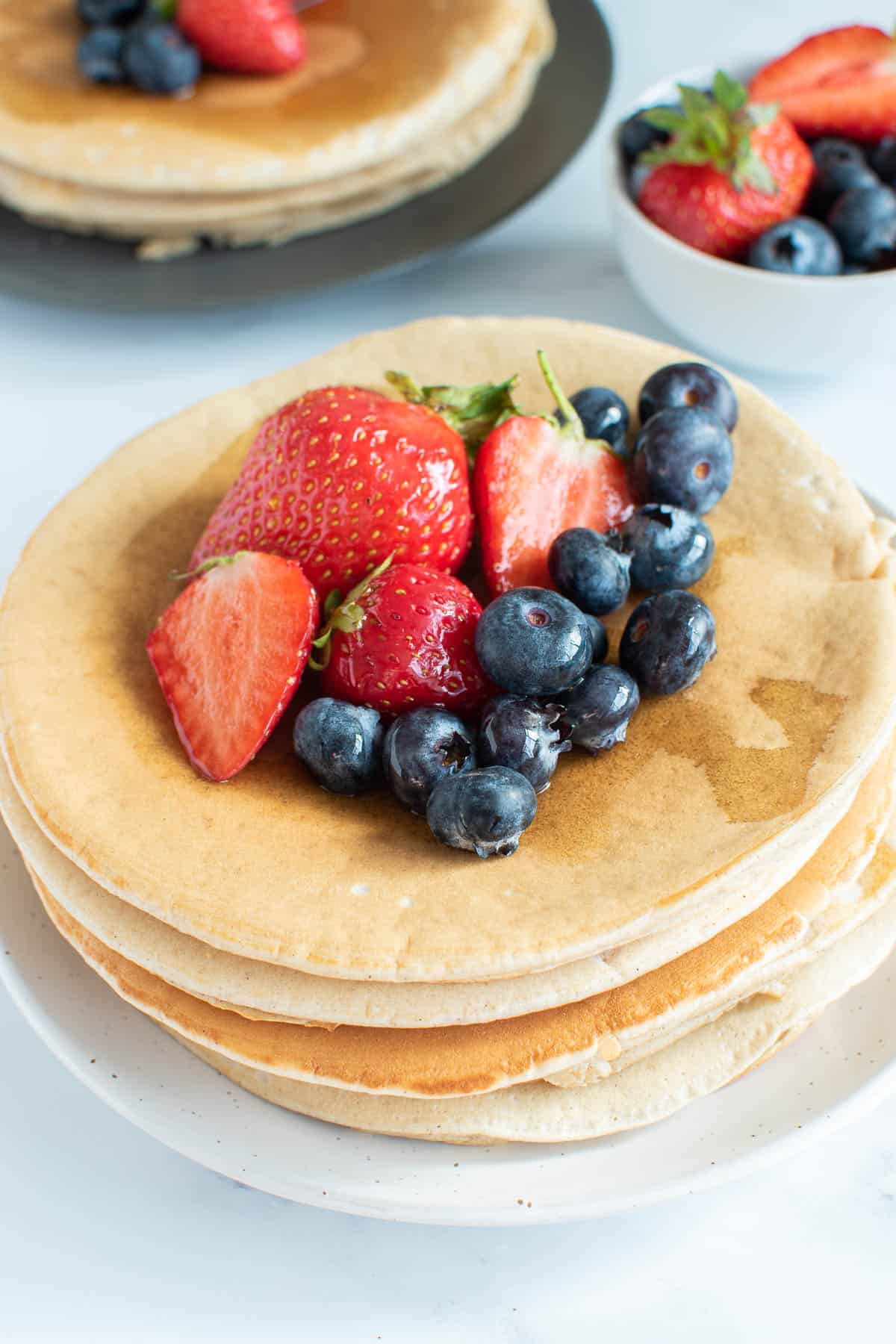 Golden American oat milk pancakes on a plate, with blueberries and strawberries on top.