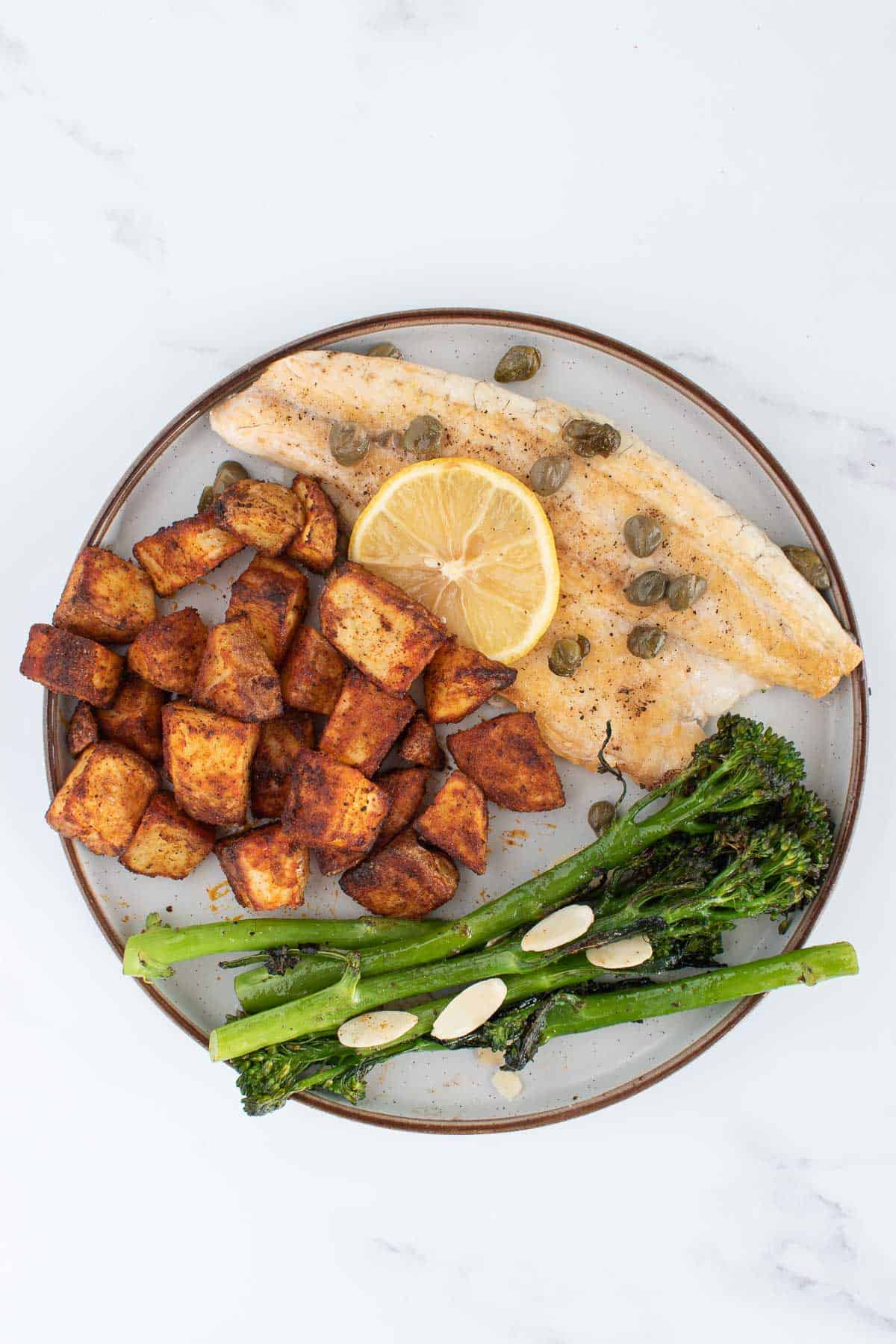 A plate with pan seared sea bass, roasted potatoes and roasted broccoli.