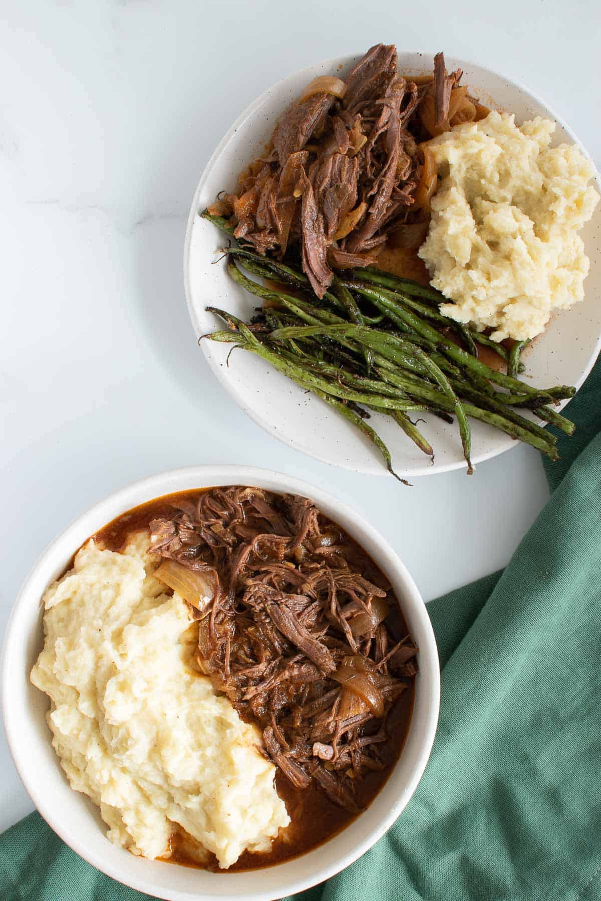 Two plates with slow cooked braising steak with mashed potatoes and green beans.