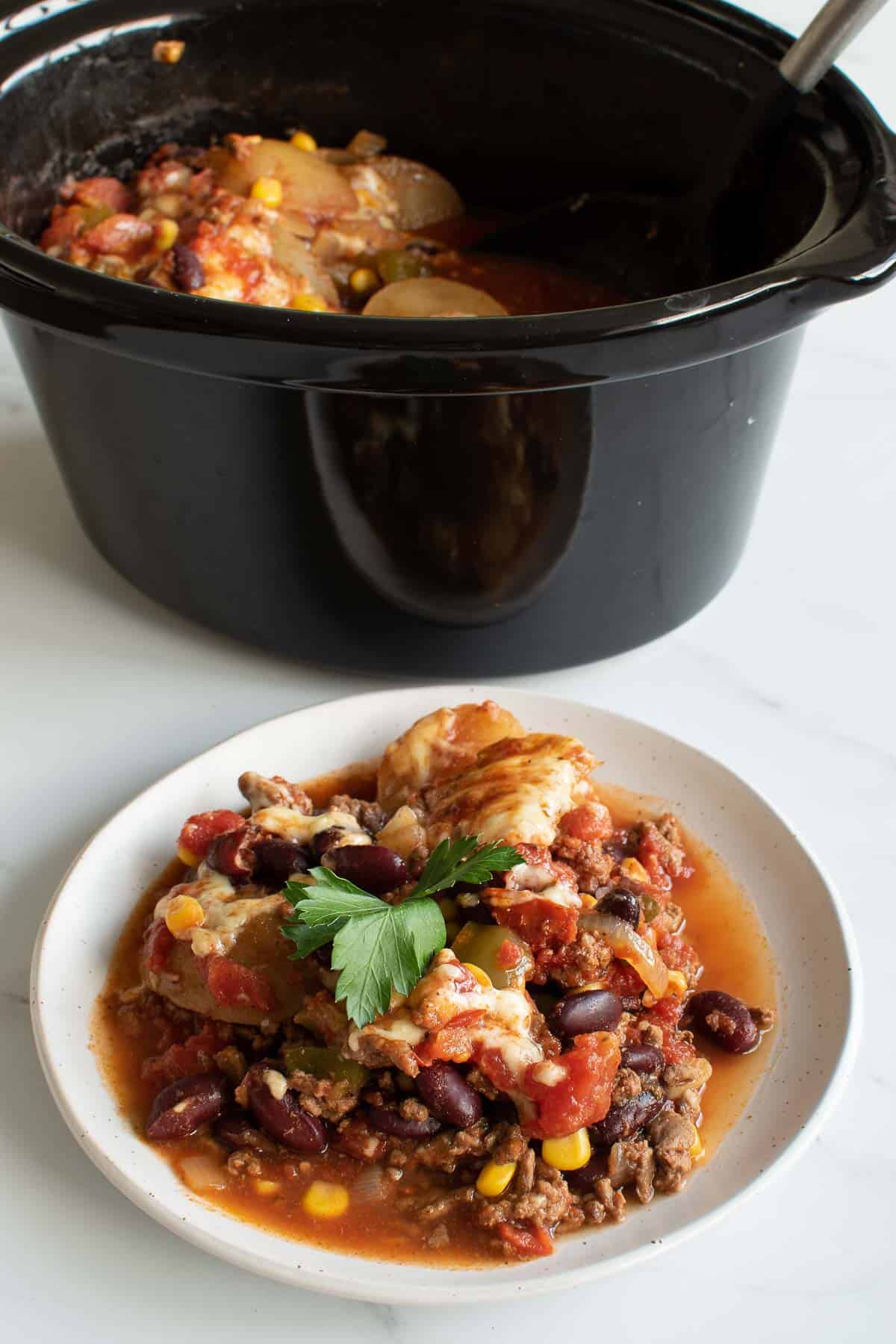 A plate of cowboy casserole in front of a crockpot.