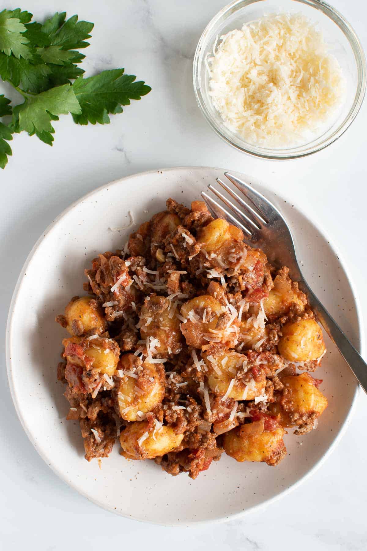 Gnocchi bolognese on a plate, with Parmesan on the side.