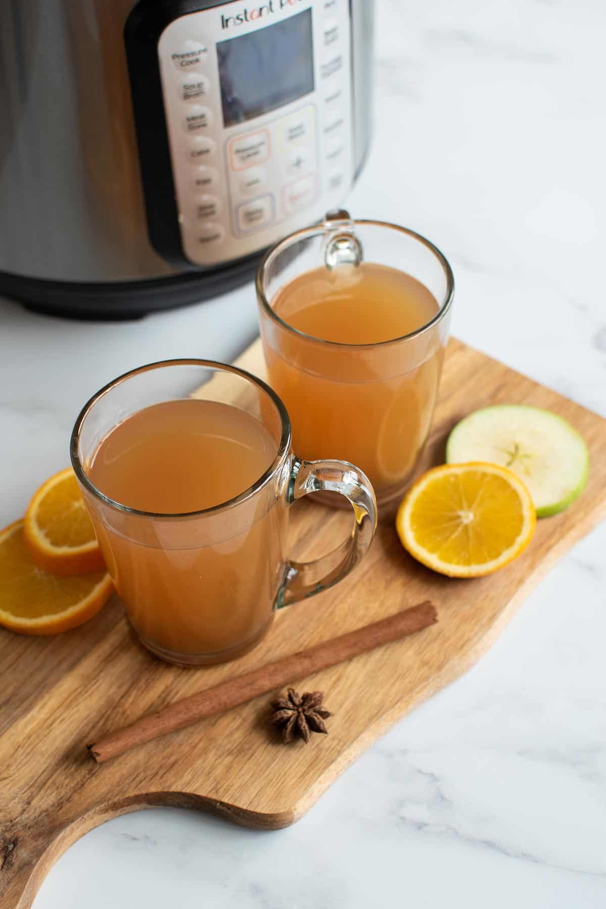 Two glasses of hot mulled cider with cinnamon, star anise and oranges.