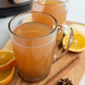 Glasses filled with hot cider, with cinnamon sticks and orange slices on the side.