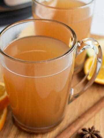 Glasses filled with hot cider, with cinnamon sticks and orange slices on the side.