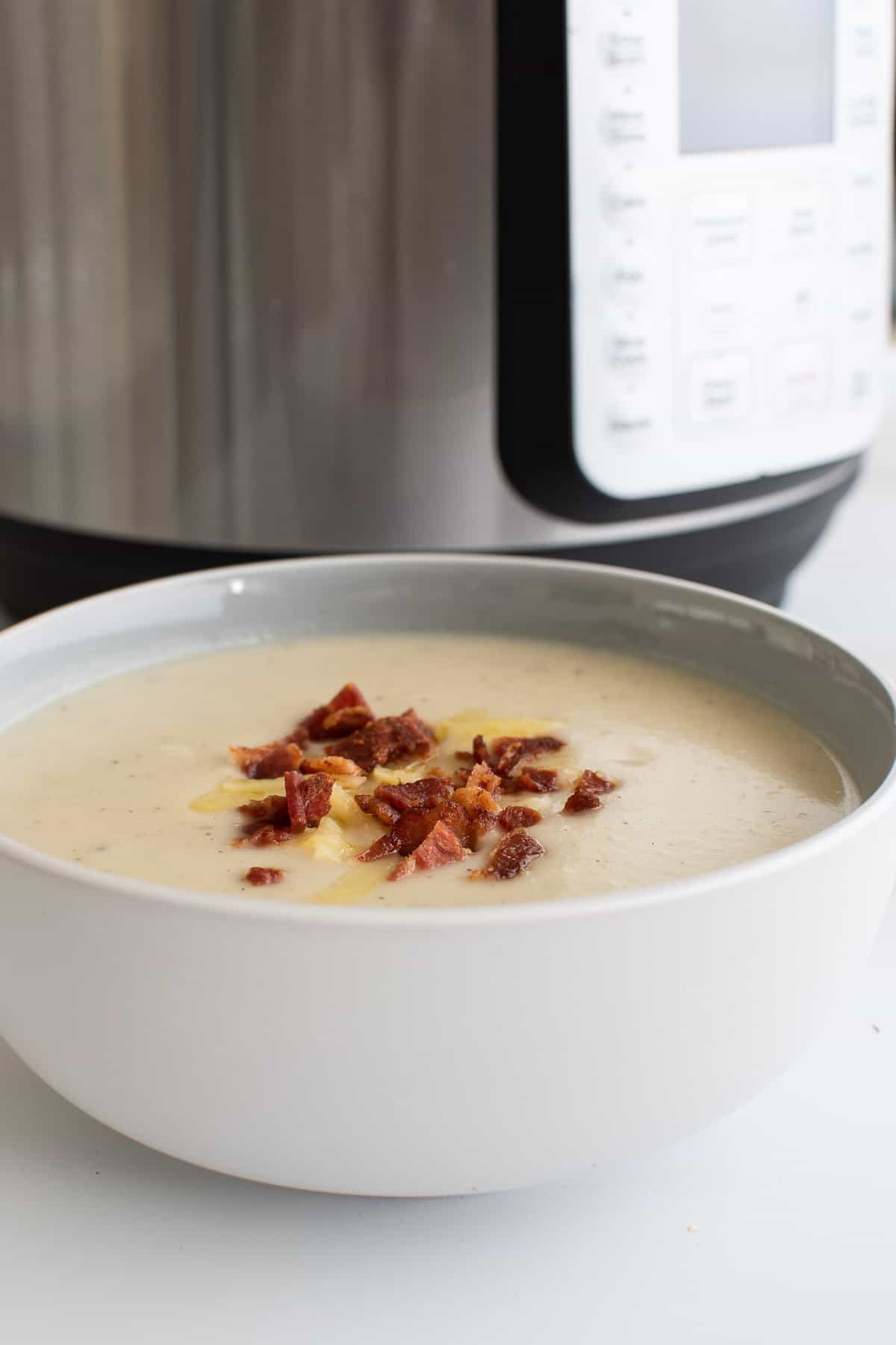 A bowl of cauliflower soup in front of an Instant Pot.