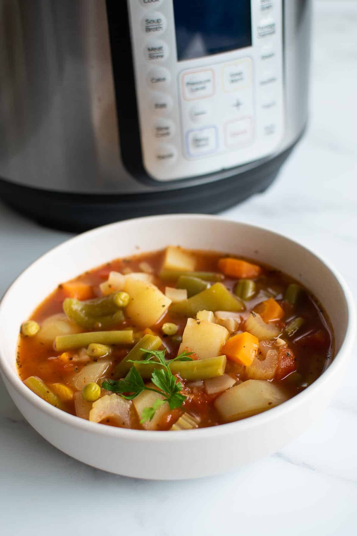 A bowl of vegetable soup in front of Instant Pot.