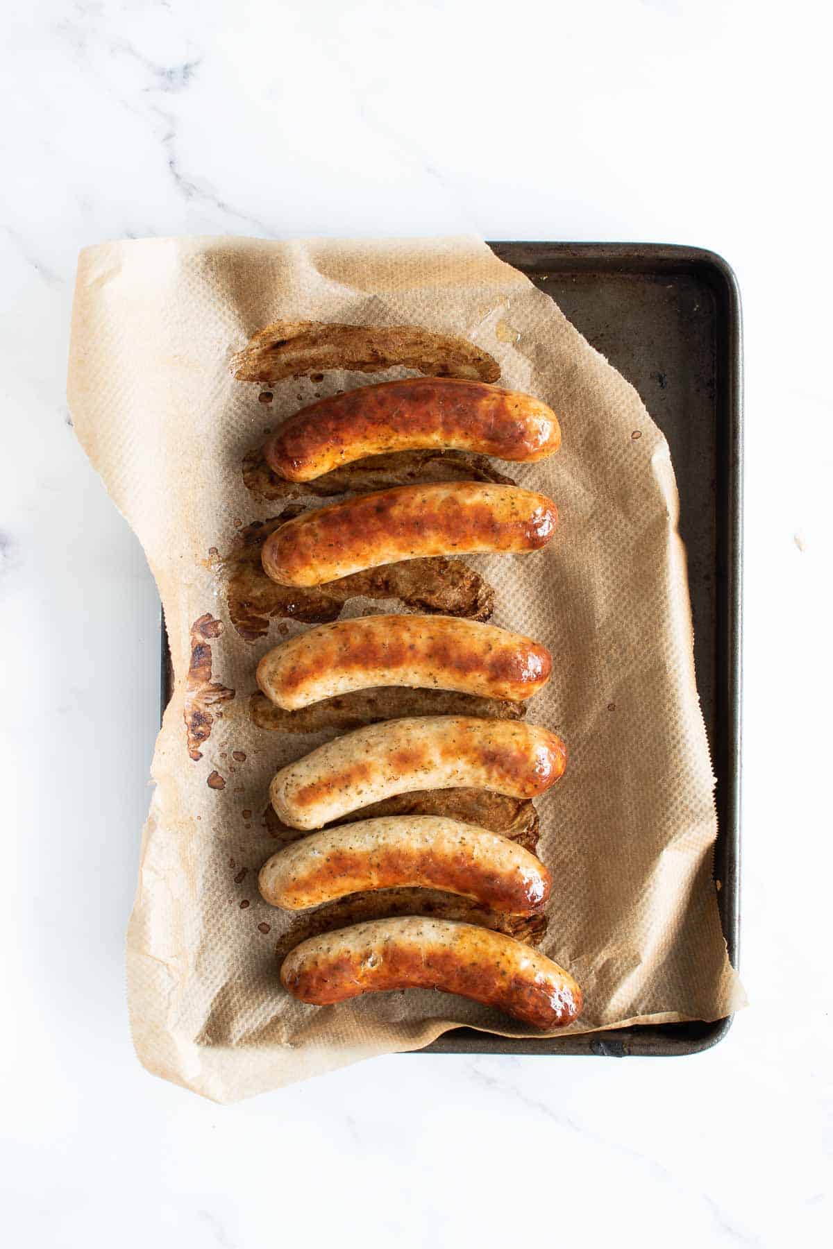 6 cooked bratwurst sausages on a baking sheet.