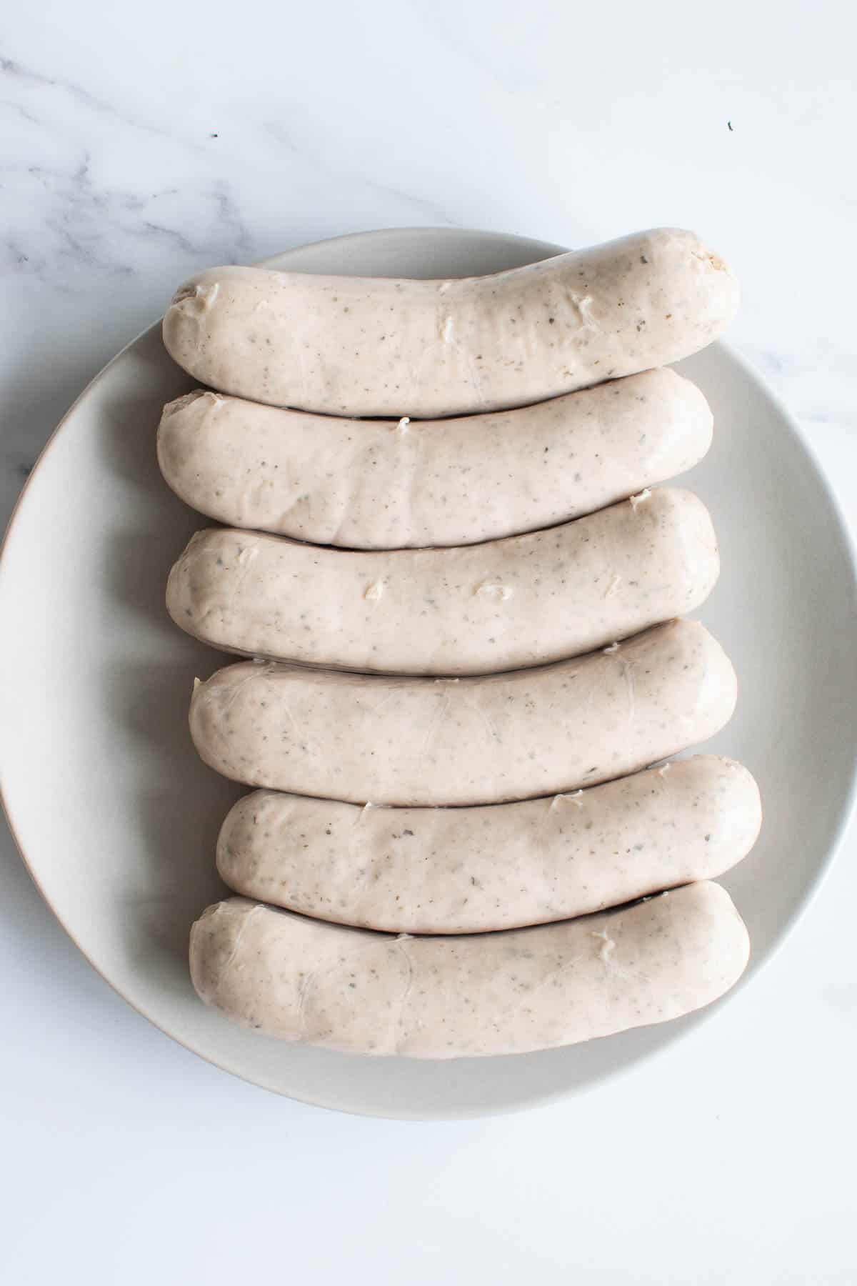 Raw bratwurst sausages on a plate.